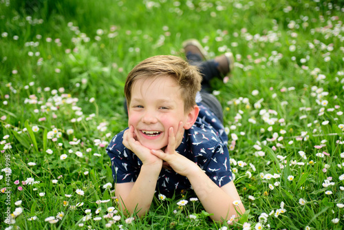 Smiling boy lying on carefree flower field. Cute kid child enjoying on field and dreaming.