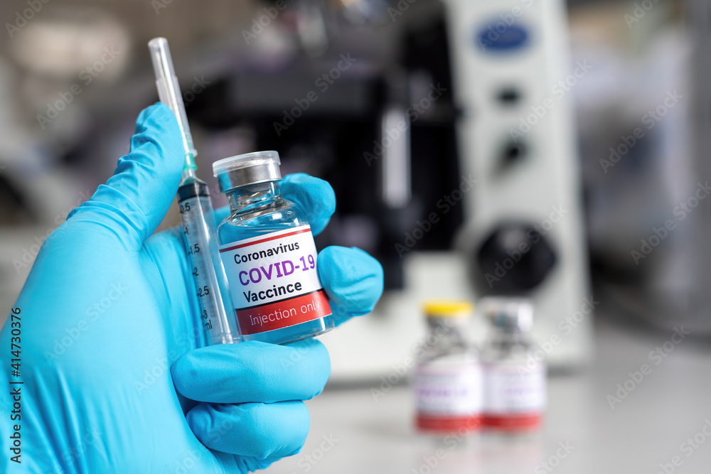 The covid-19 coronavirus vaccine concept, a blue-gloved hand holding a syringe and vial of the COVID-19 vaccine in a medical science laboratory.