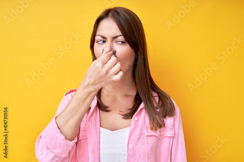Girl pinched her nose with fingers, concept of unpleasant smell of sweat and bad breath, isolated in yellow studio