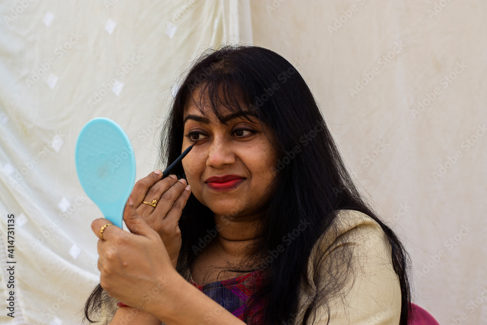 A beautiful Indian lady getting ready while applying lipstick and holding a mirror on her hand. A beautiful Indian lady getting ready while applying lipstick and holding a mirror on her hand.