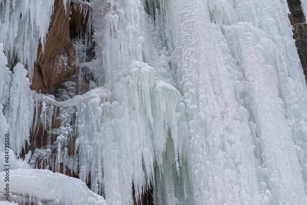 Frozen stream of water on the background of a rocky surface. Bizarre ice. White, aquamarine shades. The concept of a frozen waterfall. Frozen stream of water on the background of a rocky surface. Bizarre ice. White, aquamarine shades. The concept of a frozen waterfall.