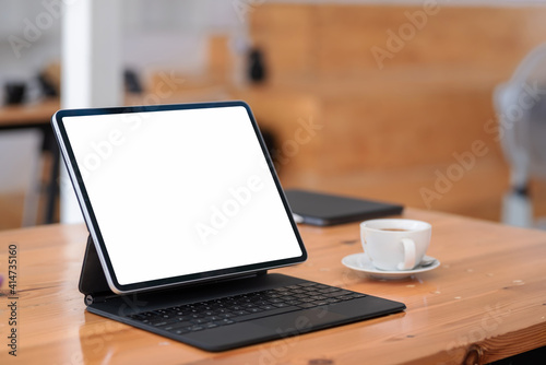 Mock up tablet blank screen with a coffee mug placed at the table in office.