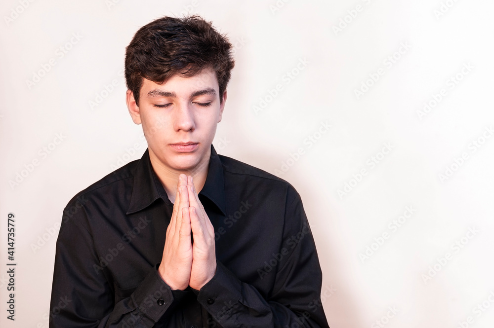 A young boy with a sad face and closed eyes holds his hands in prayer and prays that his parents, family will be healthy A young boy with a sad face and closed eyes holds his hands in prayer and prays that his parents, family will be healthy