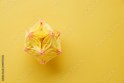 Multicolor handmade modular origami ball or Kusudama Isolated on yellow background. Visual art  geometry  art of paper folding  paper crafts. Top view  close up  selective focus  copy space.