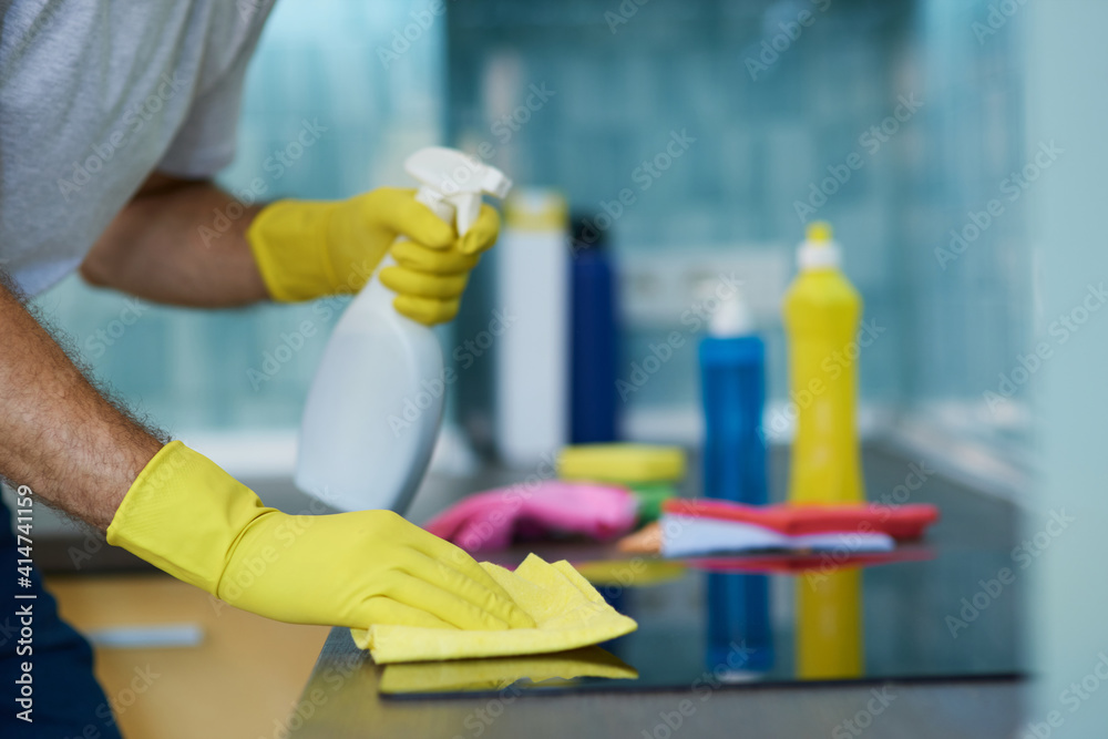 Neat Cleaning. Close up shot of hands of man, professional male cleaner wearing gloves, using spray detergent while cleaning oven in the kitchen