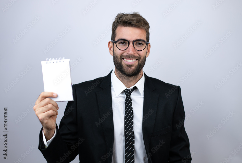 Young business man wearing suit smiling and showing blank notebook Young business man wearing suit smiling and showing blank notebook