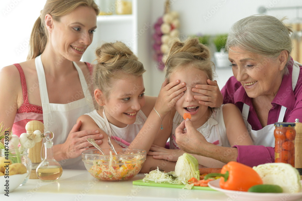 Cute girls with mother and grandmother preparing delicious fresh salad in kitchen Cute girls with mother and grandmother preparing delicious fresh salad in kitchen