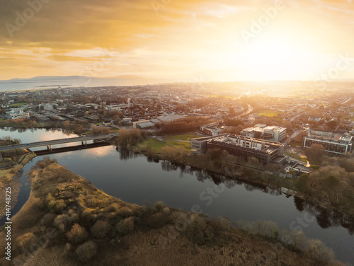 Aerial drone view on Sunset over Galway city, Bridge over River Corrib and NUI buildings, Atlantic ocean in the background. West coast of Ireland. Warm sunny cloudy sky, Sun flare
