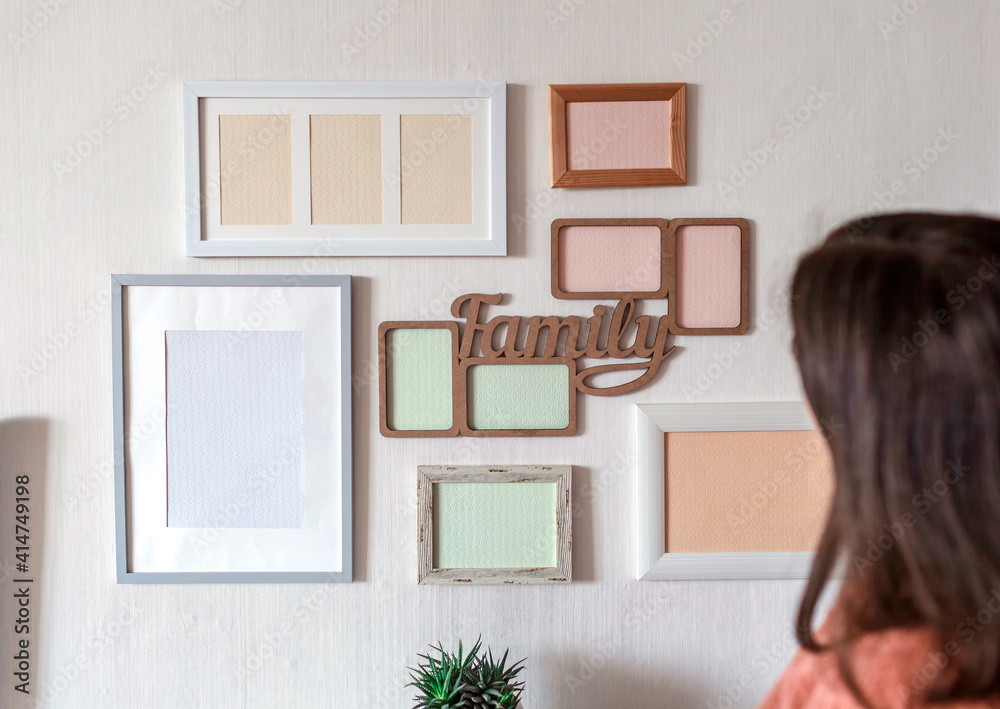 Girl hanging frame on white wall with set of different empty vertical and horizontal picture frames to create family photo gallery, to capture a moment, mockup template on white background, lifestyle Girl hanging frame on white wall with set of different empty vertical and horizontal picture frames to create family photo gallery, to capture a moment, mockup template on white background, lifestyle