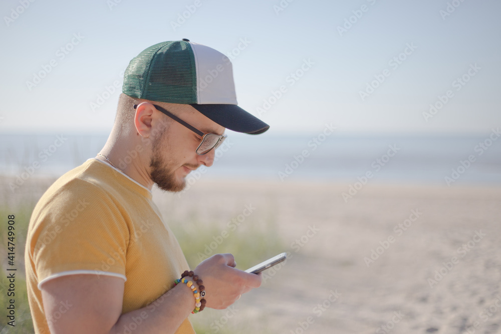 young bearded man looking at phone at the beach.