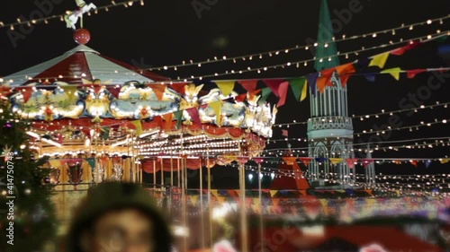 Big carousel on the Red Square.Christmas market in the city.People have fun together on holidays.Multicolored flag garland, fir tree and Kremlin tower on background