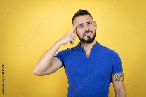 Handsome man with beard wearing blue polo shirt over yellow background smiling and thinking with his fingers on his head that he has an idea.
