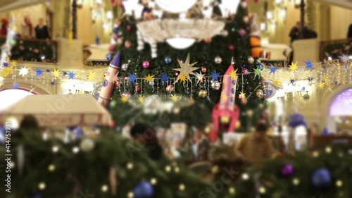  Crowded restaurant in mall new year holidays. Big green christmas tree with giant balls and rocket toys.People blurred and unrecognizable
