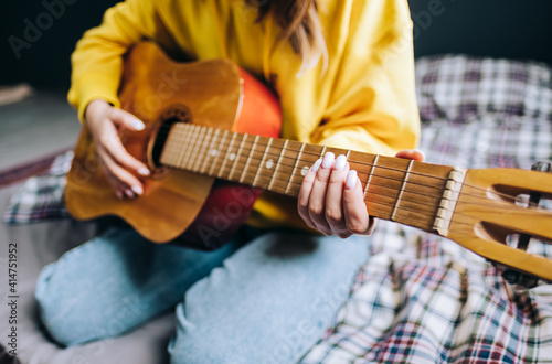 Closeup young woman's hand playing acoustic guitar at home.