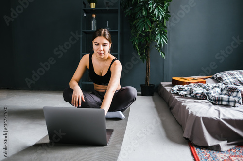 Beautiful brunette fitness woman make stretching exercises in front laptop, doing yoga indoors at home. Staying fit and healthy photo