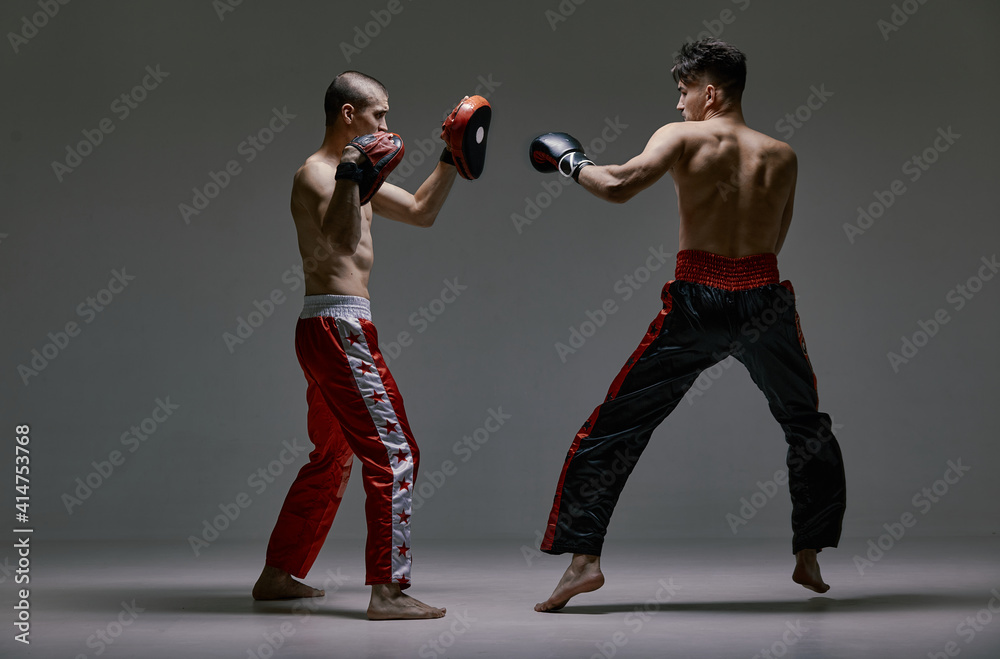 Athletic males in boxing gloves training martial arts technique. Fighting guys during mixed fight workout