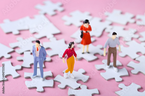 Miniature people with white jigsaw puzzles on pink background