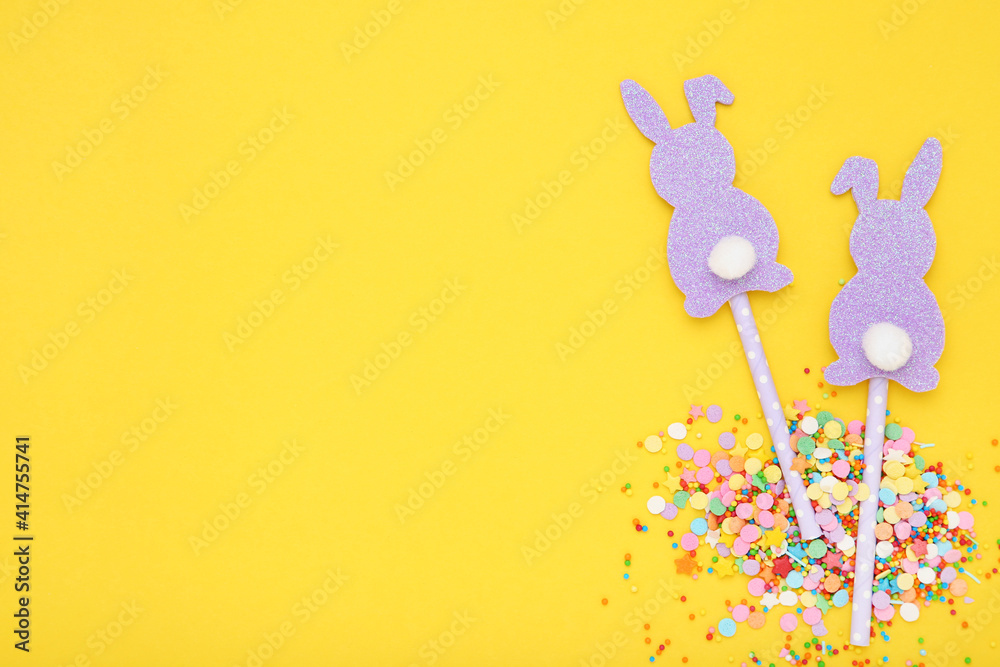 Easter concept. Paper rabbits with colorful sprinkles and confetti on yellow background