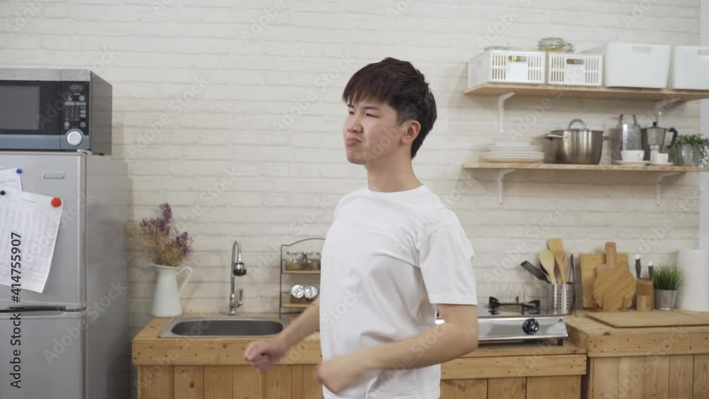 tired asian man standing in the kitchen is stretching his body and extending arms to the side to circling his wrist and staring afar in contemplation. tired asian man standing in the kitchen is stretching his body and extending arms to the side to circling his wrist and staring afar in contemplation.