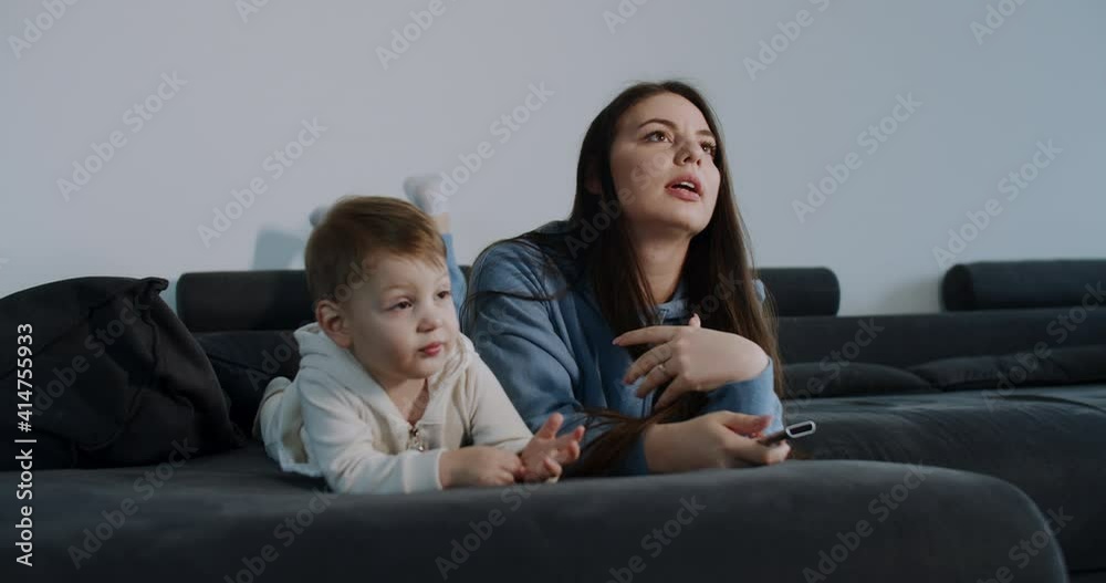 mother and young child, son, are lying on the bed and watching TV. Slow motion. mother and young child, son, are lying on the bed and watching TV. Slow motion.