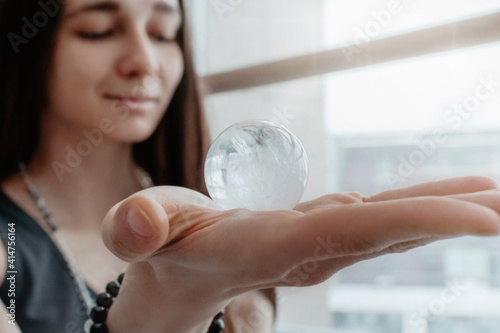 Woman in grey clothes smiles and holds in her hands semiprecious sphere , object for religious rituals, meditations and alternative medicine. Girl looks at amazing mineral ball