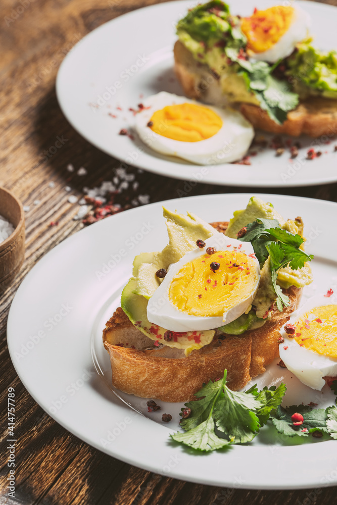 Poached egg and avocado on sliced toasted bread, two plates, top view Poached egg and avocado on sliced toasted bread, two plates, top view