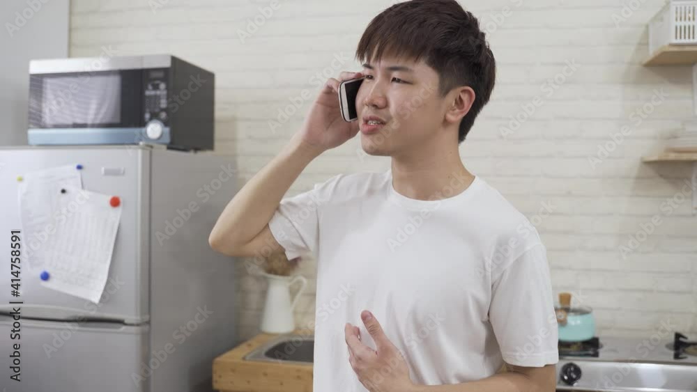 portrait asian male is raising and spreading his arm while talking unhappily on the smartphone in a home interior with white brick wall. portrait asian male is raising and spreading his arm while talking unhappily on the smartphone in a home interior with white brick wall.