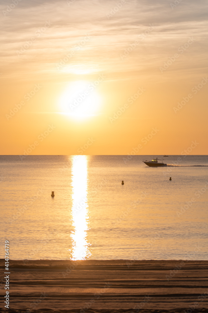 boat sailing at sunrise with the beach in the foreground