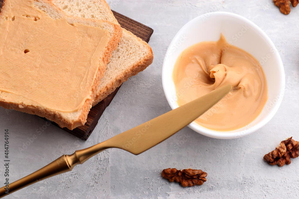 White bowl with natural walnut paste, golden knife, walnut and toast sandwiches on a light background. Traditional vegetarian breakfast close up White bowl with natural walnut paste, golden knife, walnut and toast sandwiches on a light background. Traditional vegetarian breakfast close up