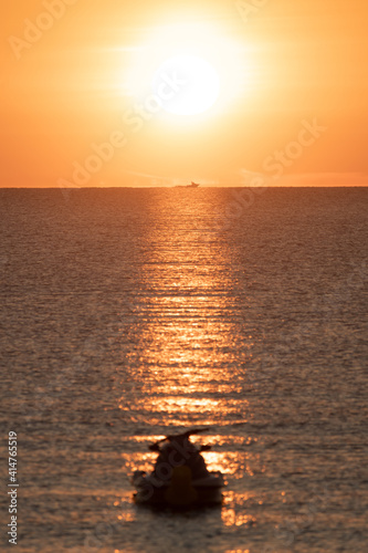 Sunrise with jet ski in foreground and fishing boat in background sailing