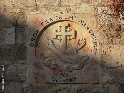Catholic coat of arms of the Order of the Brothers of the Minarets on the wall of a school in the ancient city of Acre in Israel close-up.