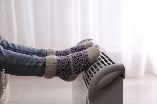 Child warming feet on electric heater at home, closeup