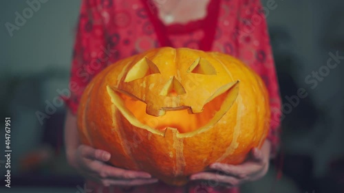 a woman is holding a large pumpkin with eyes and mouth carved out, and a candle is burning inside the pumpkin. the concept of fear at the Helluin holidays photo