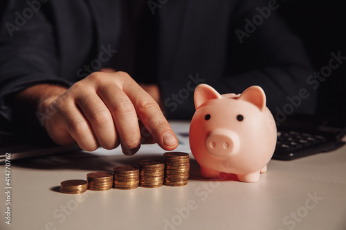 Man calculates profit, piggy bank with stack of coins at the desk. Savings and investment concept.
