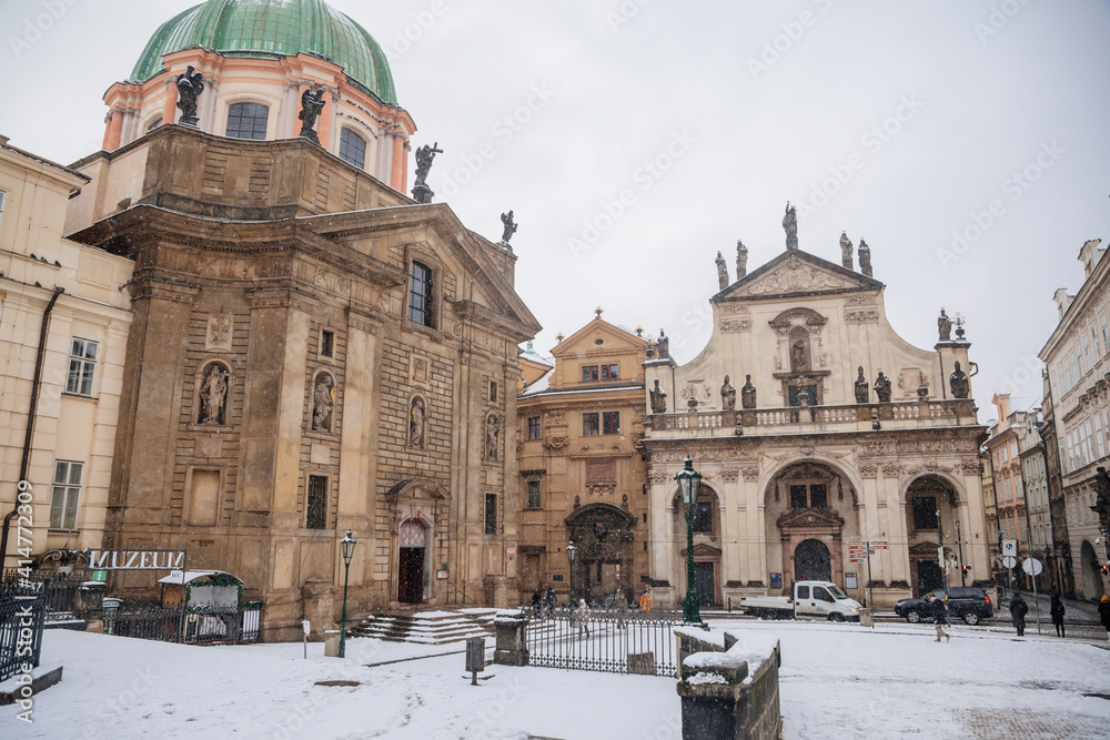 Knight of the Cross Square near Charles Bridge under snow in winter day, Baroque Church of St. Francis of Assisi and Church of the Blessed Savior, Old town, Prague, Czech Republic
