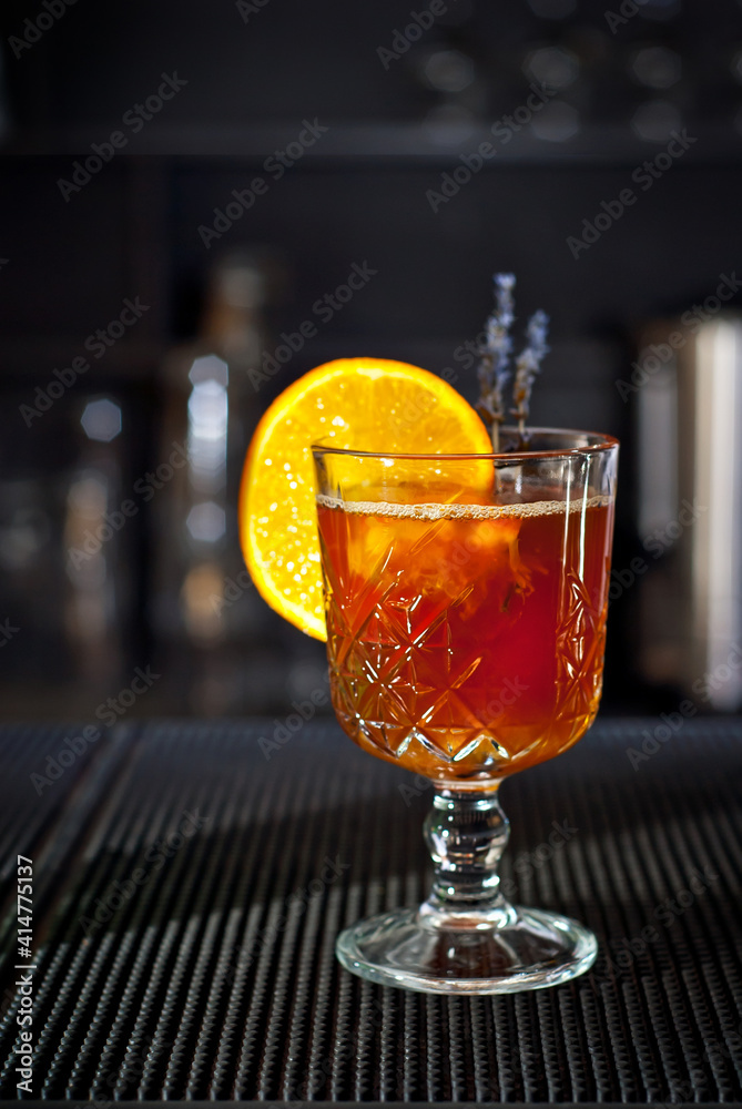 Orange cocktail on the bar. Mulled wine with white wine. Shelves with bottles of alcohol blurred in the background.