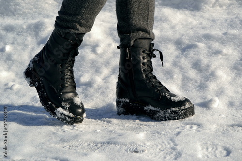 Woman's legs in high black boots walking down the street in snow
