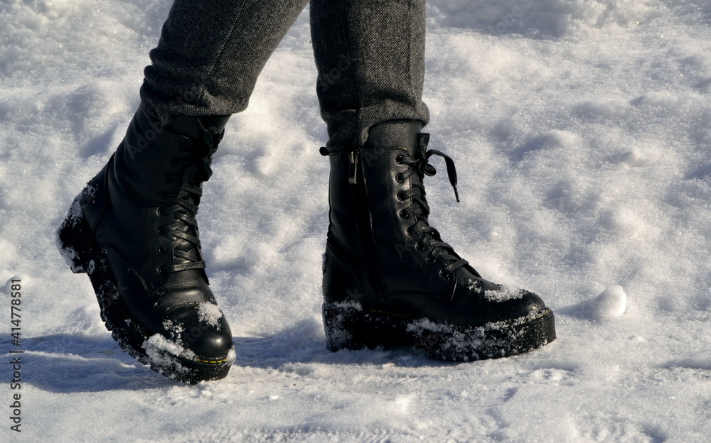 Woman's legs in high black boots walking down the street in snow Woman's legs in high black boots walking down the street in snow