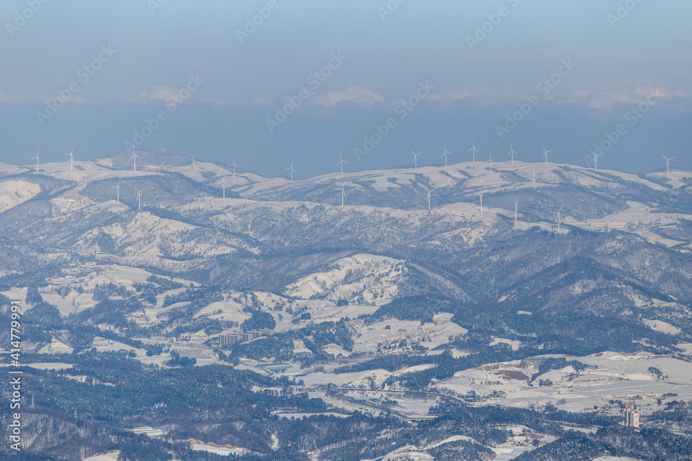 Alpencia, South Korea, 2016, winter - General plan. White windmills stand on top of snow-capped mountains.