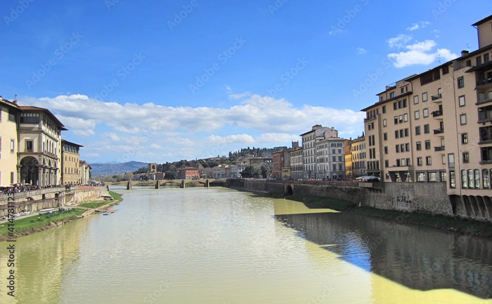 View of the Arno River in Florence, Italy. Yellow water. A bridge in the distance, buildings on the sides 