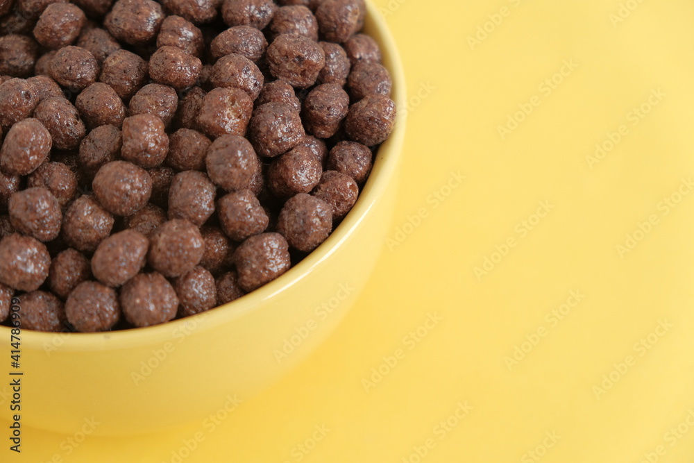 Chocolate cereal corn balls in a yellow bowl on a yellow background. Top view. Copy, empty space for text Chocolate cereal corn balls in a yellow bowl on a yellow background. Top view. Copy, empty space for text