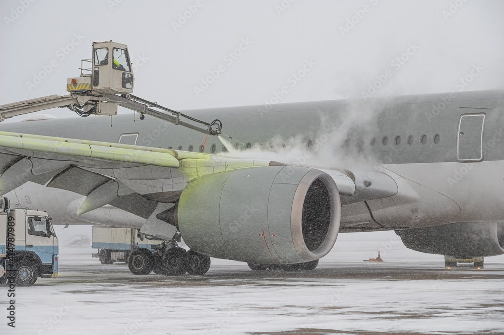 Winter at the airport. Snow storm. Airplane de-icing before take off. De-icing  the aircraft before the flight. The de-icing machine sprinkles the wing of  a passenger plane with de-icing fluid. Stock Photo