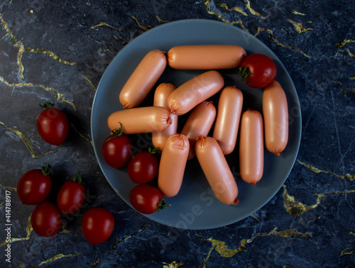 Appetizing sausages on a grey plate on a dark marble background, close up
