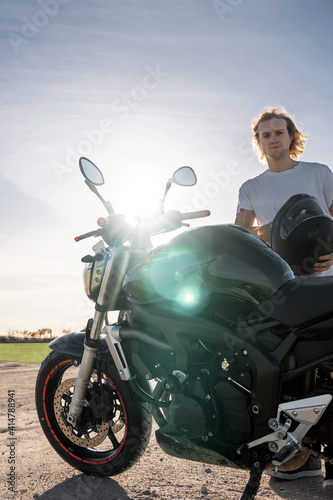 blond caucasian man with helmet and black motorcycle with sunlight