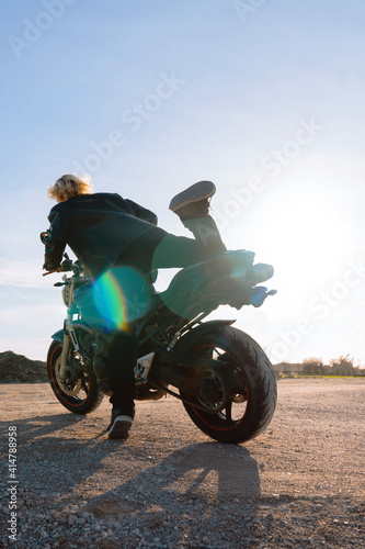 blond man riding on black motorcycle with sun reflections