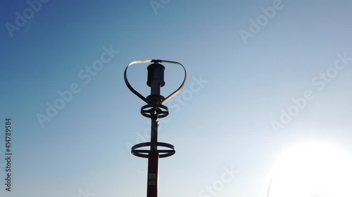 Vertical axis wind turbine utilize renewable wind energy while spinning against blue sky.
