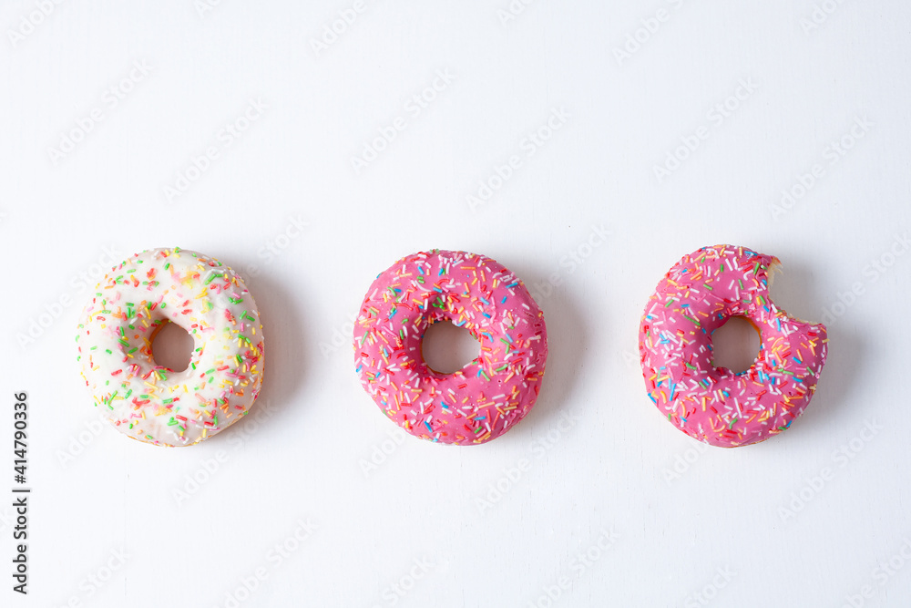Three doughnuts two pink and white, one bitten on a white background overall plan Three doughnuts two pink and white, one bitten on a white background overall plan