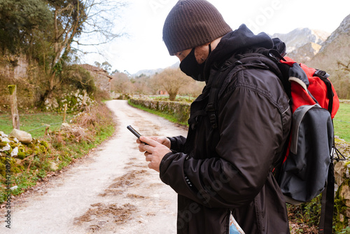 man consulting maps on his smart phone while doing mountain route. Person with a mask against the coronavirus. New normal.