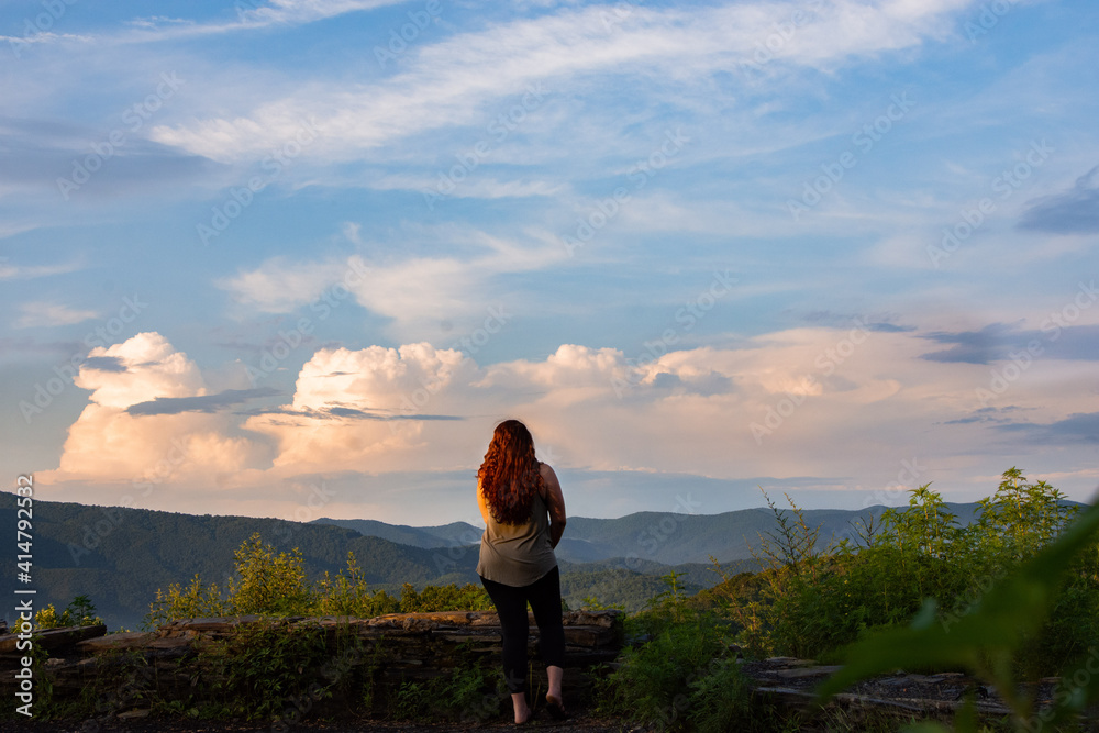 Woman looking out over a beautiful mountain view with puffy clouds in the blue sky.