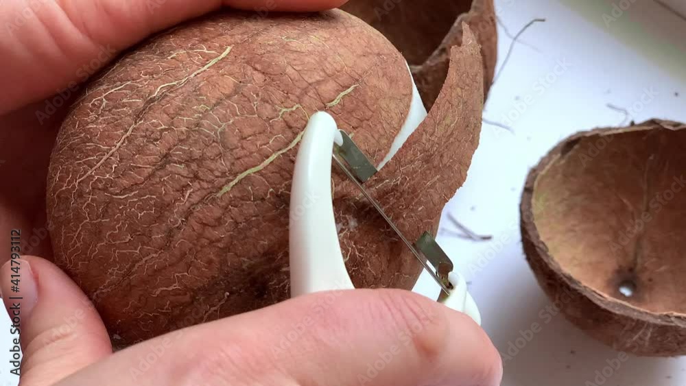Method for peeling coconut flesh. A woman peels the skin of a coconut with a vegetable peeler.